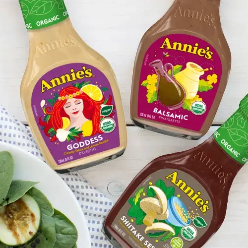 Three bottles of Annie’s Natural Salad Dressing next to a green salad